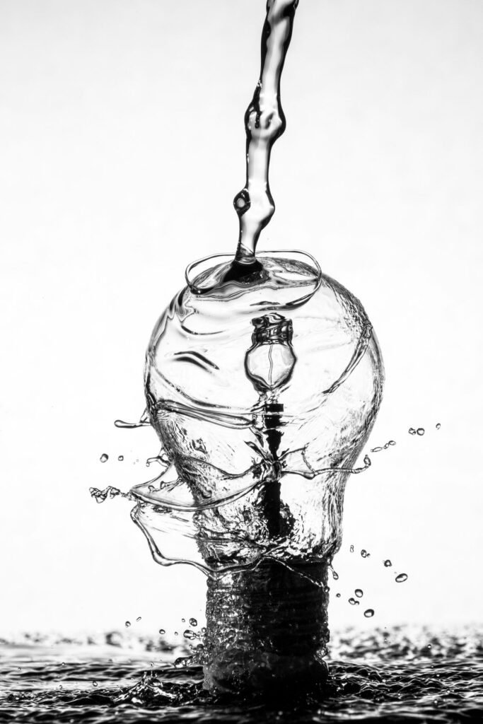 Black and white photo of water pouring down on light bulk - for my blog post about water, hydration and alchemy